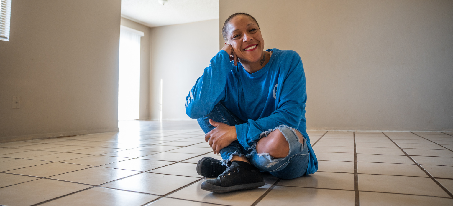 candice-move-in Woman sitting on the floor in an empty room smiling at the camera